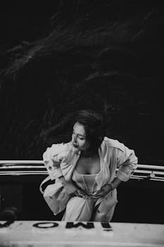 Artistic black and white portrait of a woman standing on a boat with a dramatic pose.
